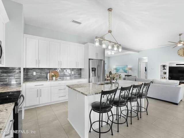 kitchen with decorative light fixtures, appliances with stainless steel finishes, an island with sink, light stone countertops, and white cabinets