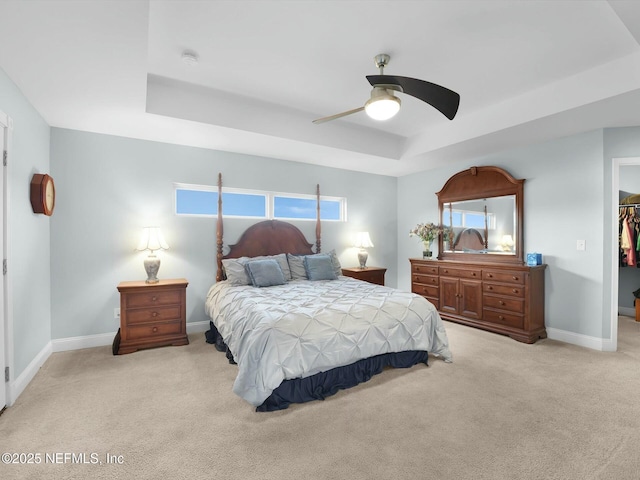 bedroom featuring light carpet, a tray ceiling, multiple windows, and a spacious closet