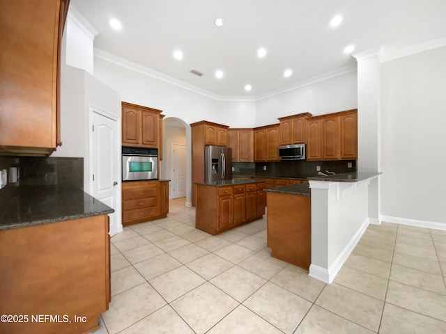 kitchen featuring ornamental molding, stainless steel appliances, a kitchen island, and dark stone counters