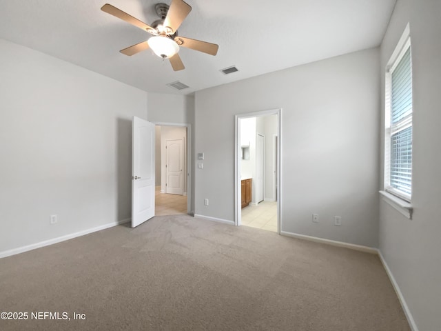 unfurnished bedroom featuring ceiling fan, light colored carpet, and ensuite bath