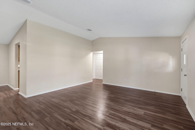 empty room with vaulted ceiling, a textured ceiling, and dark hardwood / wood-style flooring