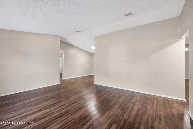 empty room featuring dark hardwood / wood-style flooring, vaulted ceiling, and a textured ceiling