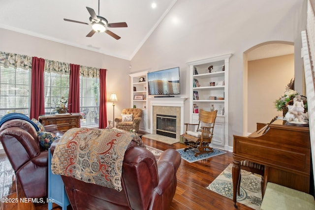 living room featuring arched walkways, a fireplace, wood finished floors, a ceiling fan, and crown molding