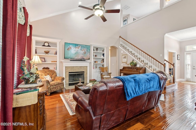 living area featuring built in features, a tiled fireplace, ornamental molding, wood finished floors, and stairs