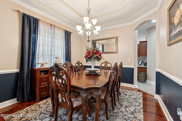 dining space with arched walkways, a chandelier, baseboards, dark wood-style floors, and a raised ceiling