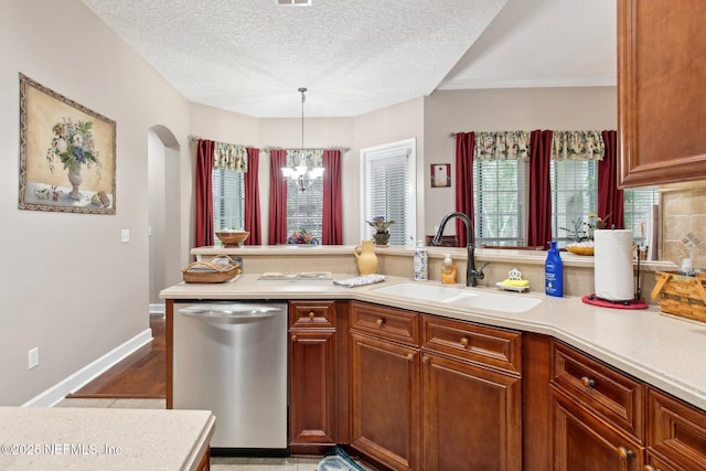 kitchen with dishwasher, light countertops, a sink, and a notable chandelier