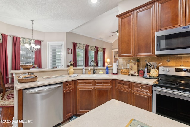 kitchen with stainless steel appliances, a peninsula, a sink, light countertops, and backsplash