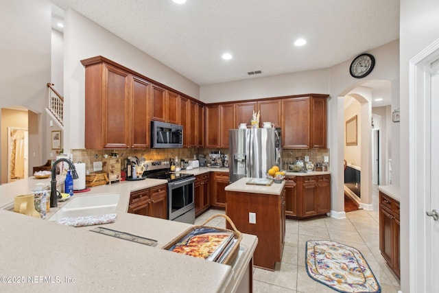 kitchen with arched walkways, light tile patterned floors, a sink, light countertops, and appliances with stainless steel finishes