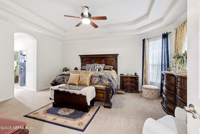 bedroom with a tray ceiling, baseboards, arched walkways, and carpet