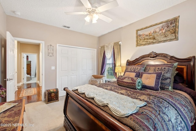 carpeted bedroom featuring a ceiling fan, a textured ceiling, visible vents, and a closet