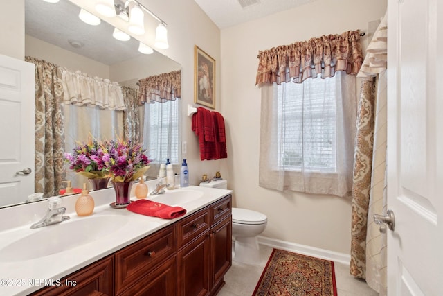 bathroom with toilet, double vanity, baseboards, and a sink