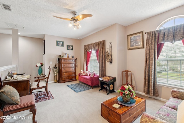 living room with baseboards, visible vents, light colored carpet, ceiling fan, and a textured ceiling