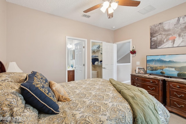 carpeted bedroom with a textured ceiling, connected bathroom, visible vents, and a ceiling fan