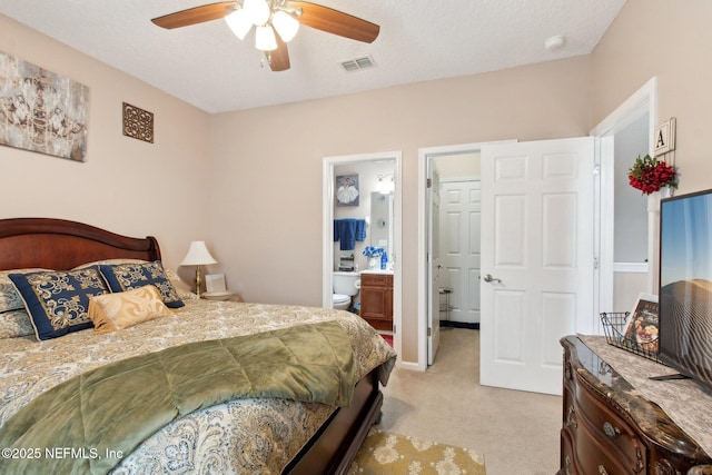 bedroom featuring visible vents, ensuite bathroom, light carpet, ceiling fan, and a textured ceiling