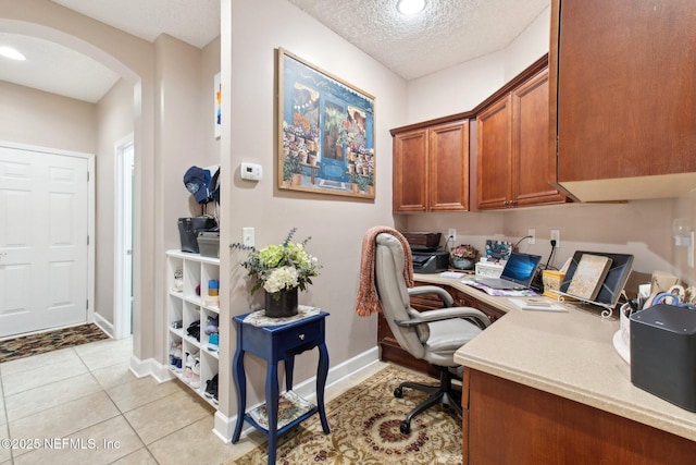 home office featuring arched walkways, light tile patterned floors, a textured ceiling, baseboards, and built in study area