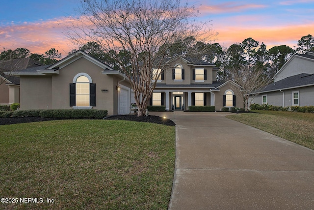 traditional home with a garage, concrete driveway, a front lawn, and stucco siding