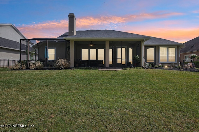 back of house with a lawn, fence, a sunroom, and stucco siding