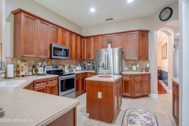 4250 Eagle Landing Pkwy, Orange Park, FL 32065 - kitchen featuring appliances with stainless steel finishes, arched walkways, light countertops, a center island, and tasteful backsplash