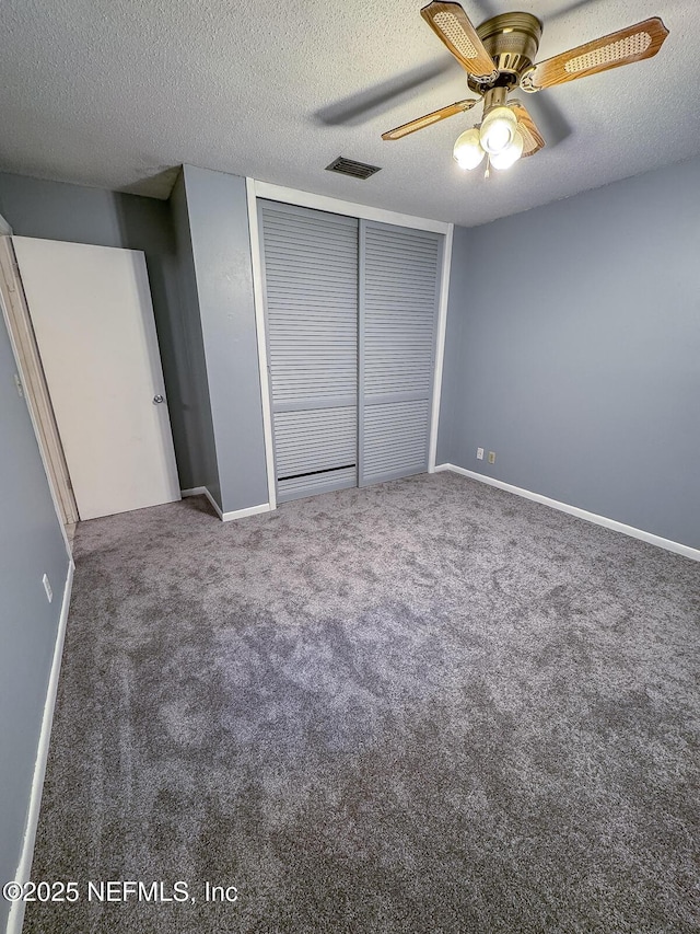 unfurnished bedroom featuring dark carpet, a textured ceiling, a closet, and ceiling fan