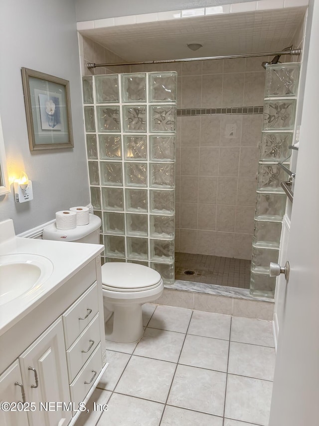 bathroom featuring tile patterned flooring, vanity, toilet, and tiled shower