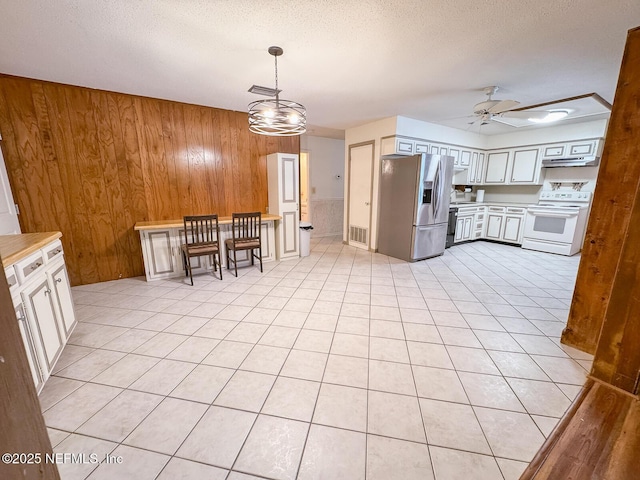 kitchen featuring white electric range oven, wood walls, stainless steel fridge with ice dispenser, hanging light fixtures, and white cabinets