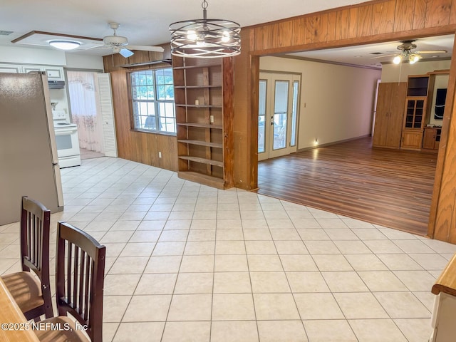 unfurnished dining area with light tile patterned flooring, wooden walls, and ceiling fan with notable chandelier