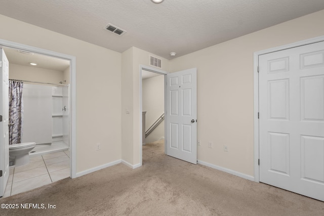 unfurnished bedroom with light colored carpet, connected bathroom, and a textured ceiling