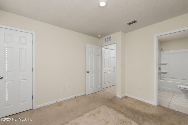 unfurnished bedroom featuring connected bathroom, light carpet, and a textured ceiling