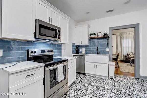 kitchen with appliances with stainless steel finishes, sink, decorative backsplash, and white cabinets