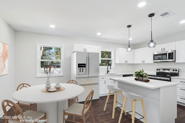 kitchen featuring a kitchen island, appliances with stainless steel finishes, sink, white cabinets, and hanging light fixtures