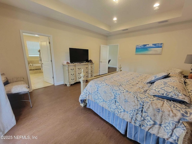 bedroom with connected bathroom, a tray ceiling, and wood-type flooring