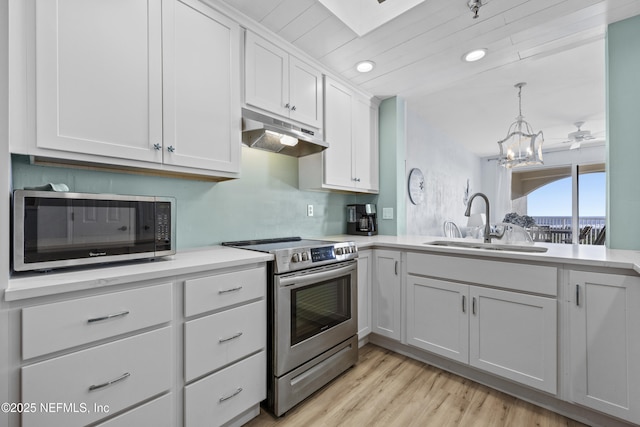 kitchen featuring appliances with stainless steel finishes, decorative light fixtures, white cabinetry, sink, and light hardwood / wood-style flooring