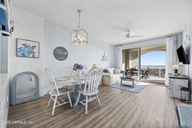 dining space with ceiling fan with notable chandelier and light hardwood / wood-style flooring