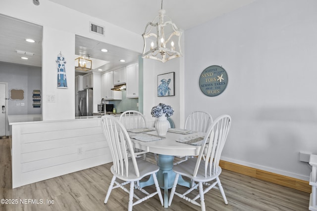 dining space with sink, light hardwood / wood-style flooring, and a notable chandelier