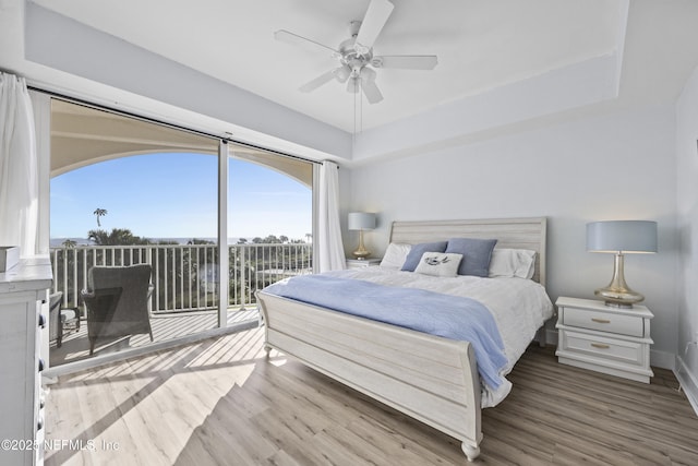 bedroom featuring ceiling fan, wood-type flooring, a tray ceiling, and access to outside