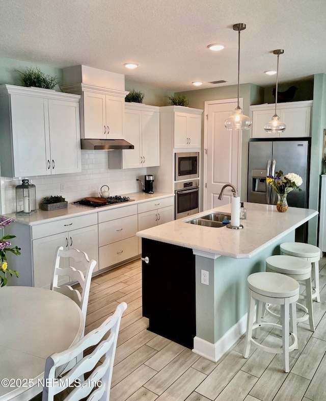 kitchen featuring sink, white cabinetry, hanging light fixtures, stainless steel appliances, and a kitchen island with sink