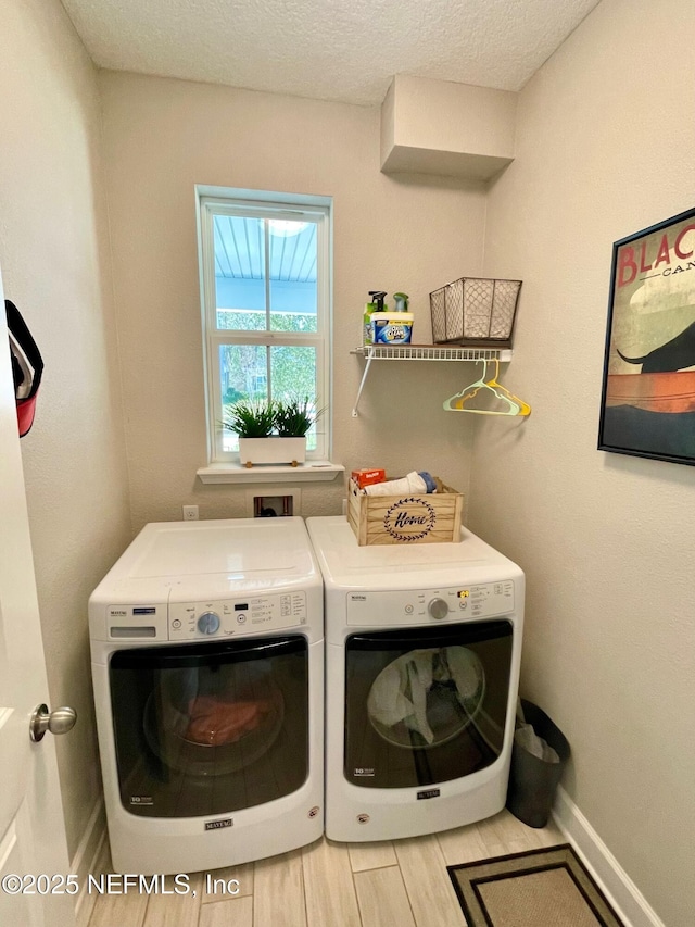 laundry room with light wood-type flooring, a textured ceiling, and washer and clothes dryer