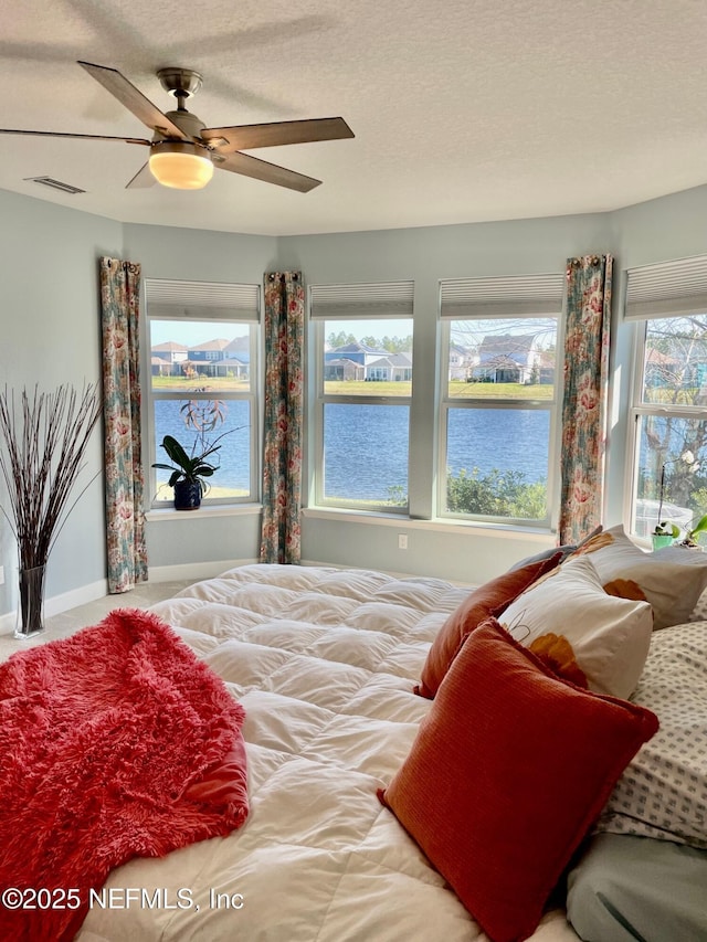 bedroom featuring ceiling fan, a textured ceiling, and a water view