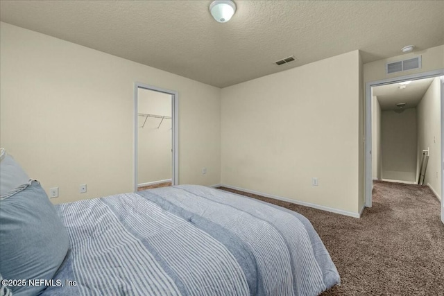 bedroom featuring a walk in closet, a closet, a textured ceiling, and carpet flooring