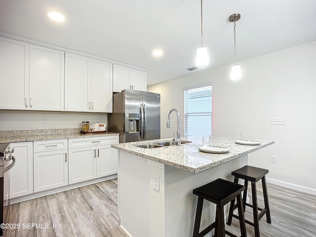 kitchen with sink, hanging light fixtures, stainless steel refrigerator with ice dispenser, white cabinets, and a center island with sink