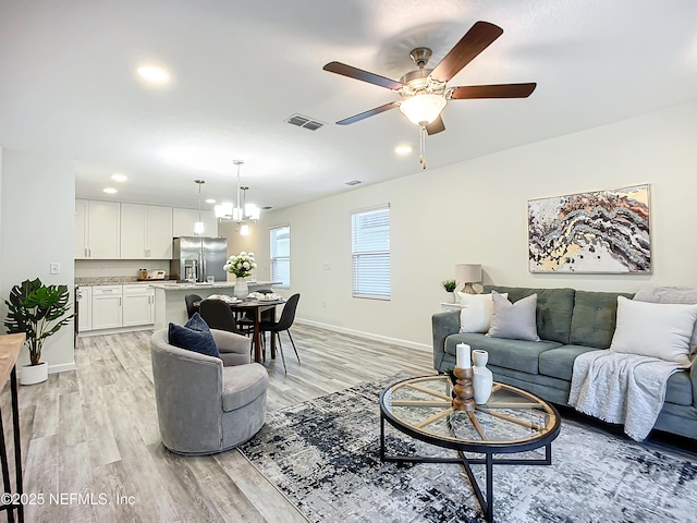 living room with ceiling fan with notable chandelier and light hardwood / wood-style flooring