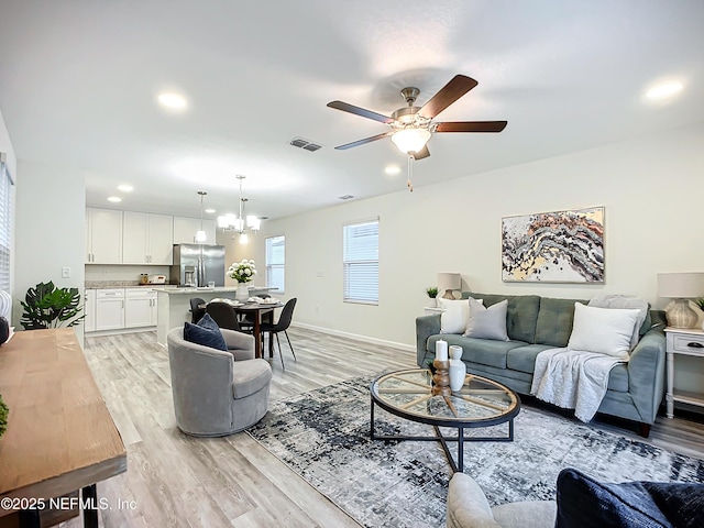 living room with ceiling fan with notable chandelier and light hardwood / wood-style floors