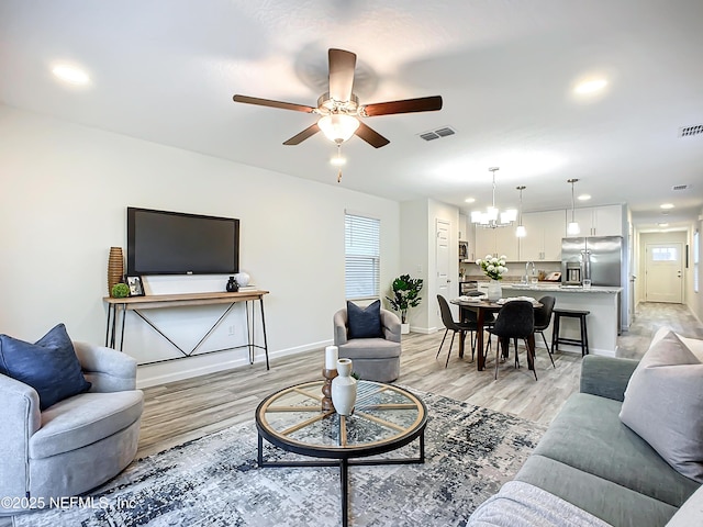 living room with sink, ceiling fan with notable chandelier, and light wood-type flooring