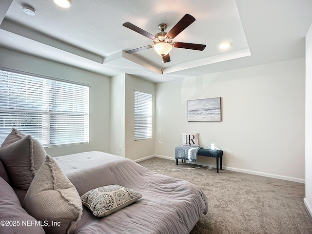 carpeted bedroom with a raised ceiling, ceiling fan, and multiple windows