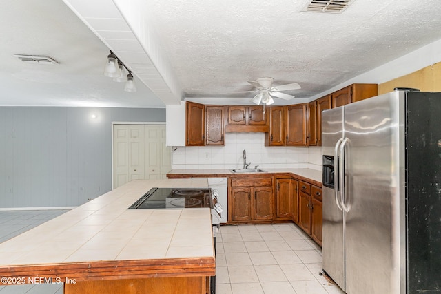 kitchen with stainless steel refrigerator with ice dispenser, light tile patterned flooring, sink, tile countertops, and backsplash