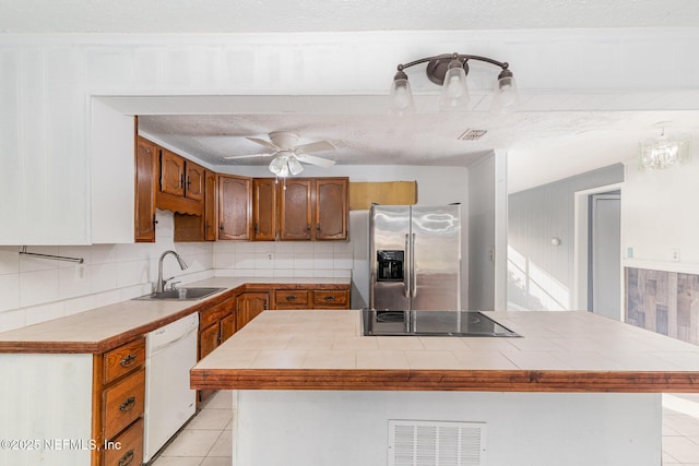 kitchen featuring tile countertops, dishwasher, sink, stainless steel fridge with ice dispenser, and a textured ceiling