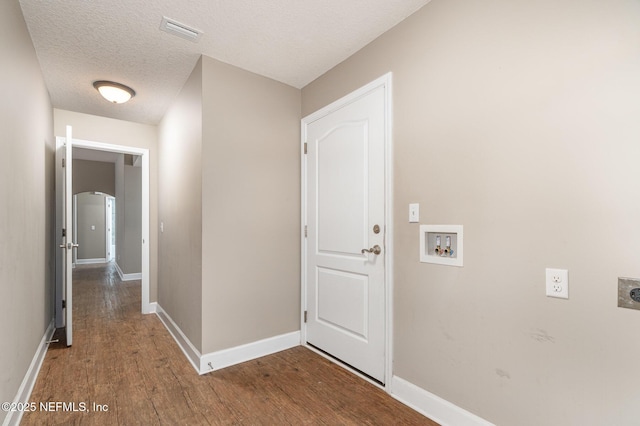 hallway with a textured ceiling, arched walkways, wood finished floors, visible vents, and baseboards