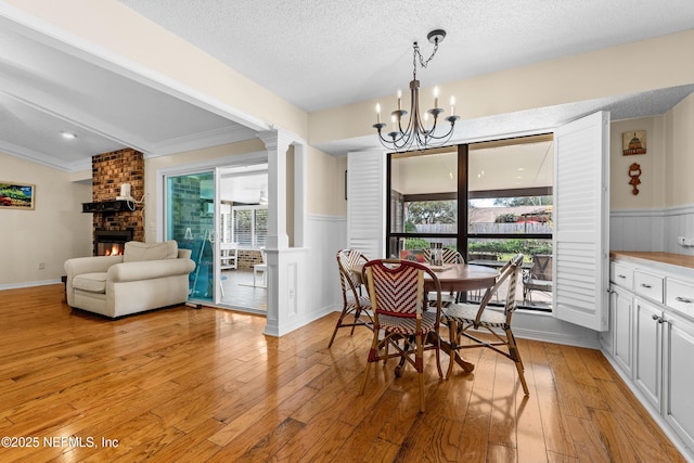 dining room with decorative columns, a textured ceiling, a brick fireplace, a chandelier, and light wood-type flooring