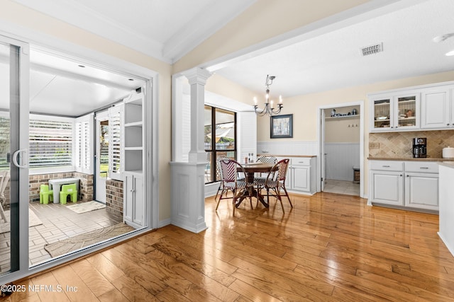 interior space with ornate columns, crown molding, decorative light fixtures, light hardwood / wood-style flooring, and white cabinets