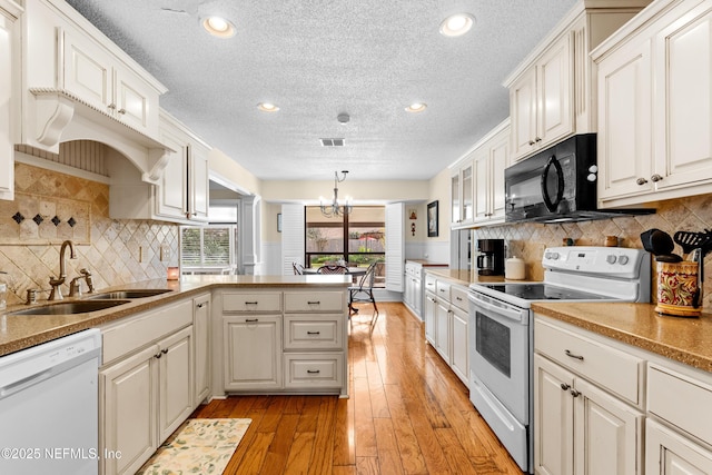 kitchen with sink, white appliances, hanging light fixtures, and white cabinets